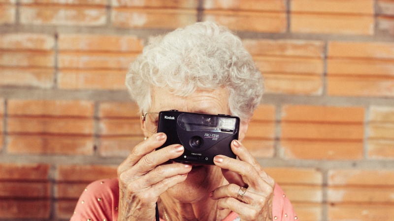 Eine ältere Frau fotografiert mit den Gegenüber mit einer Einwegkamera.