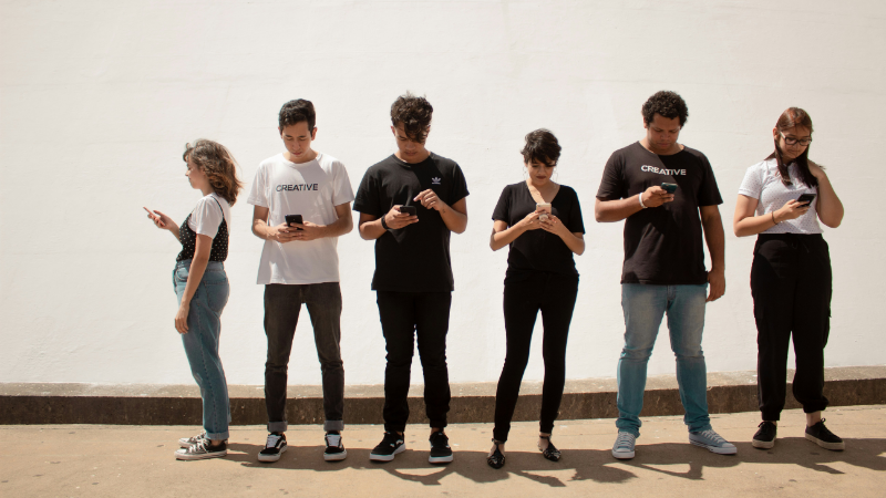 Das Foto zeigt eine Gruppe junger Menschen, die alle auf ihr Smartphone gucken. Kein Smartphone zu haben, bedeutet, von der Gesellschaft ausgegrenzt zu werden.
