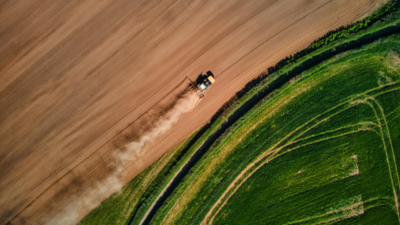 Das Bild zeigt einen Traktor von oben, der ein Feld bestellt. Eine Seite des Feldes ist grün bewachsen, die andere trocken und erdig. Das soll zeigen, dass nachhaltige KI zwar im Kampf gegen den Klimawandel nützlich sein, selbst aber auch hohe Kosten für die Umwelt verursacht.