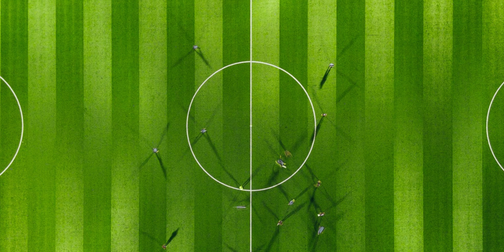 The image shows a football field from above. The players are only visible because of their shadows, symbolizing Humans in the Loop.