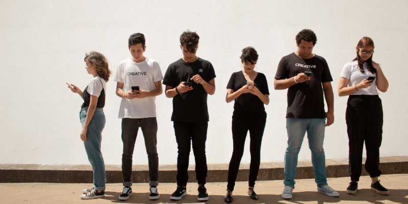 The photo shows a group of young people all looking on their mobile phones, showing that someone with No Smartphone is excluded and perceived as weird.