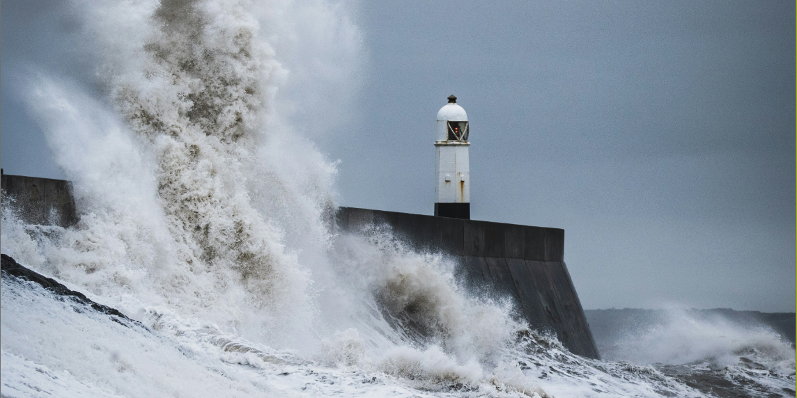 A powerful image symbolising resilience: ocean waves crashing against a lighthouse during the daytime, representing researchers standing strong against science hostility.